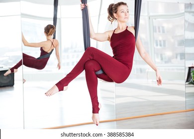 Attractive thoughtful young woman doing pose of aerial yoga using hammock - Powered by Shutterstock