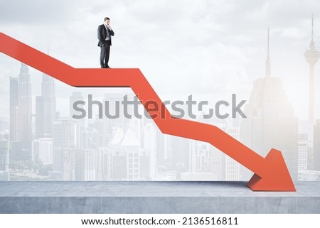 Attractive tiny european businessman standing and balancing on abstract red downward chart arrow on light city background with mock up place. Down, drop, finance and crisis concept