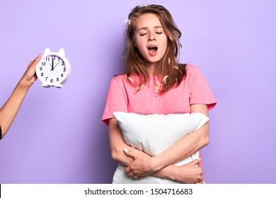 Attractive Tired Young Woman Yawning Broadly With Closed Eyes, Happy Its Time To Go To Bed, Exhausted After Long Hard Day, Invisible Person Holding Alarm Clock Showing Late Night Time.