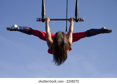 Attractive trapeze artist doing a split against a blue sky.