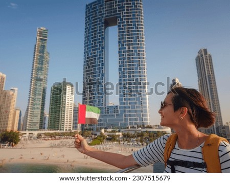 Attractive traveler asian woman with yellow backgpack walking on promenade in Dubai Marina district. Travel destinations and tourist lifestyle in UAE