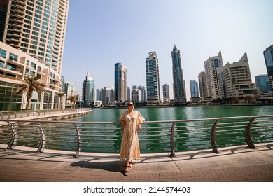 Attractive traveler woman wearing a long dress walking on a promenade in Dubai Marina district. Travel destinations and tourist lifestyle in UAE