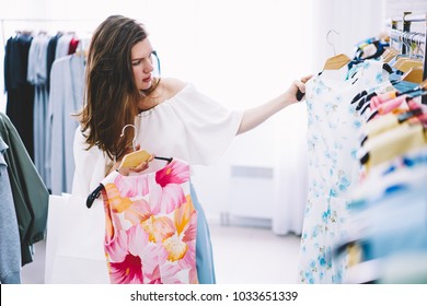 Attractive trendy dressed female customer buying clothes in botique using fitting concept while choosing.Professional stylist shopper creating trendy look concentrated on selection in designer shop