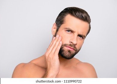 Attractive, unhappy, displeased, harsh, virile macho having problem with face, holding hand on cheek, he needs lotion, cream, mask to make soft, smooth, clear, clean skin, isolated on gray background