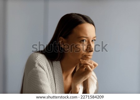 Attractive upset young woman in white bathrobe examines pimples on her face. Problematic skin on the face, acne. Portrait of girl removing pimples in the bathroom. Beauty and health of the skin.