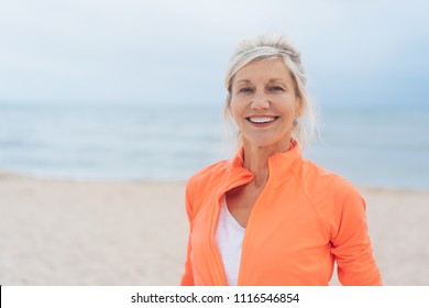 Attractive vivacious older blond woman with a beaming smile posing at the beach with ocean backdrop and copy space - Powered by Shutterstock