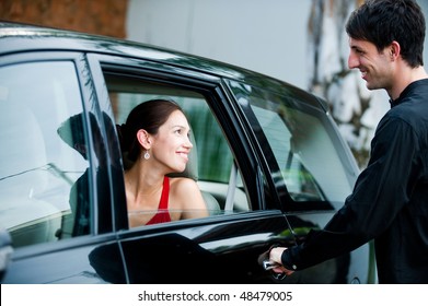 An Attractive Well-dressed Man Opening A Car Door For His Partner Outdoors