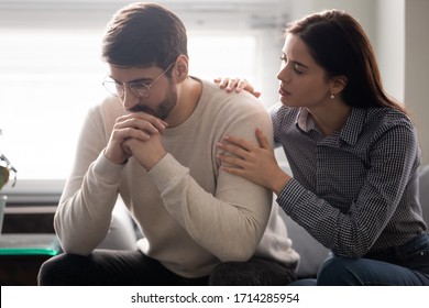 Attractive wife comforting husband embrace and showing support. Woman upset man, expressing sympathy and understanding, say sorry, family sitting on comfortable sofa at home.