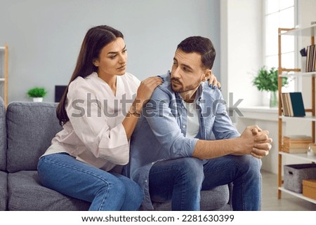 Attractive wife hugging husband from back to comfort or apologize. Young woman hugging upset man, expressing understanding, saying sorry, showing support. Couple sitting on sofa at home