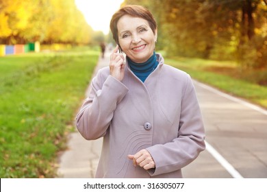 Attractive Woman 50 Years Old With Mobile Phone In The Autumn Park