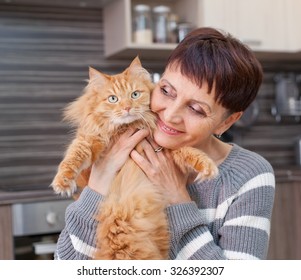 attractive woman of 50 years with a red cat in her arms at home