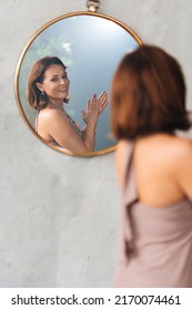 an attractive woman admires her reflection in a round mirror. feminine beauty and grooming after 40 years. cosmetics and cosmetology - Shutterstock ID 2170074461