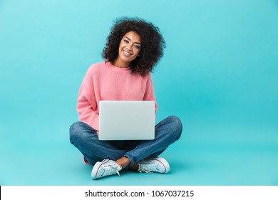 Attractive Woman With Beautiful Smile Using Silver Notebook, While Sitting In Lotus Pose On The Floor Isolated Over Blue Background