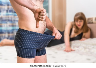 Attractive woman in bed and man in underwear is looking inside and is showing thumb down - impotence concept