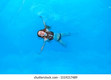 Attractive Woman In A Black Bathing Suit Floating On Her Back In The Swimming Pool And Relaxing, With Copy Space. View From The Top