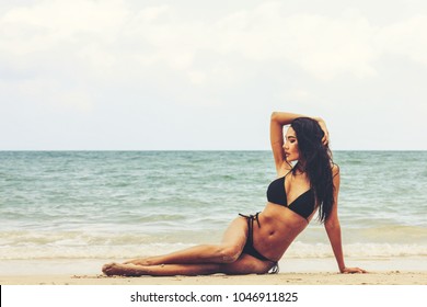 Attractive woman in black bikini with perfect body relaxing on a sand at beautiful beach in color filter with copyspace.