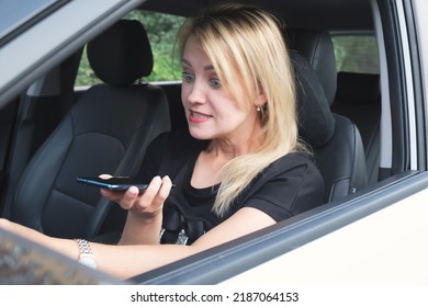 Attractive woman with blond hair sits behind the wheel of a car and speaks indignantly on the phone, holding it in front of her. Woman quarrels in a conversation on the phone.