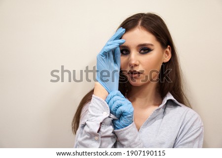 Attractive woman with blue stylish makeup putting on hands latex gloves in beauty studio