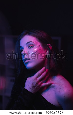 Attractive woman in bright makeup with sequins on her face in purple light with blue highlights, close-up retrieve portrait. Night party. Neon