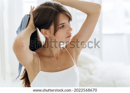 Attractive woman brushing her long brunette hair in the bathroom in the morning holding it in one hand in a ponytail as she preparing to tie a bow 
