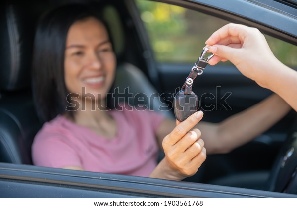 an
attractive woman in a car gets the car keys. rent or purchase of
auto - concept. professional salesperson during work with customer
at car dealership. giving keys to new car
owner.