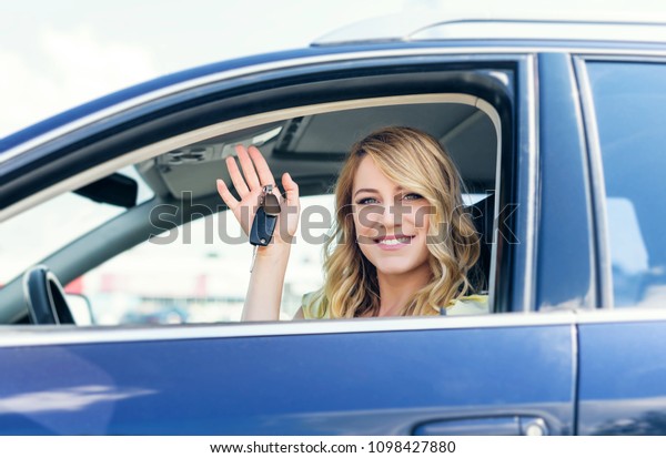 An attractive woman in a car\
holds a car key in her hand. Rent or purchase of auto -\
concept.