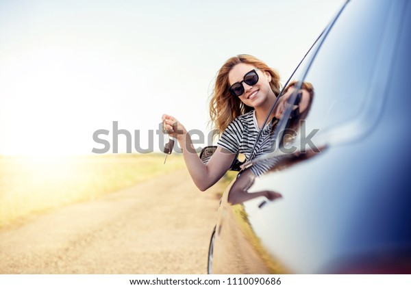 An attractive woman in a car\
holds a car key in her hand. Rent or purchase of auto -\
concept.