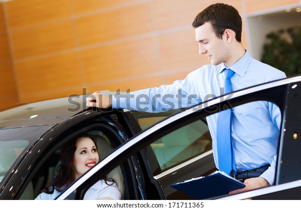 Attractive woman at car salon with consultant\
choosing a car