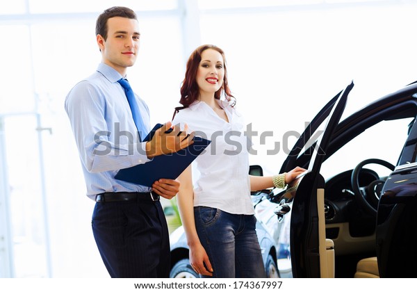 Attractive woman at car salon with consultant\
choosing a car