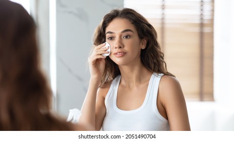 Attractive Woman Caring For Skin With Cotton Pad Applying Moisturizing Tonic Or Micellar Water Standing In Bathroom. Young Lady Cleansing Face And Removing Makeup At Home. Facial Skincare. Panorama