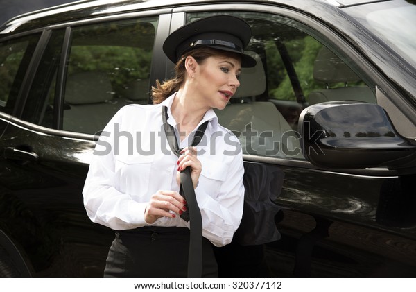 Attractive woman chauffeur tying her uniform tie in\
the wing mirror of her\
car