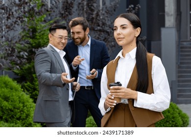 Attractive woman with coffee cup passing by two men in business suits pointing with finger and whispering behind her back. Rude males behaving unprofessional and discriminating new office worker. - Powered by Shutterstock