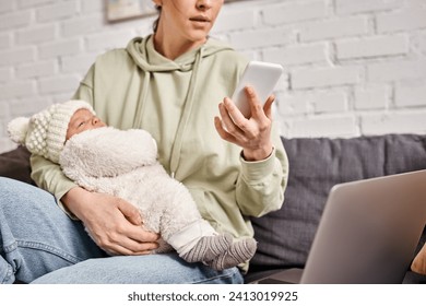 attractive woman in comfortable outfit looking at her mobile phone while holding her baby boy - Powered by Shutterstock