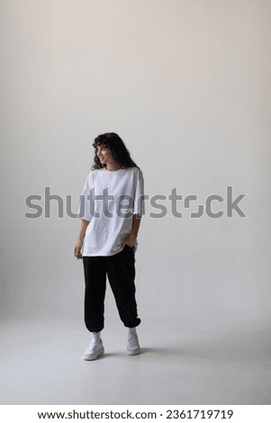 Attractive woman with curly hair wearing a white oversized t-shirt on a white background. Mock-up.