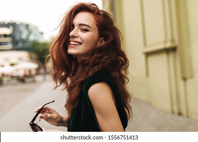 Attractive woman in dark green outfit smiling outside - Shutterstock ID 1556751413