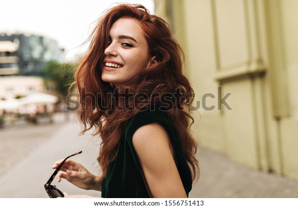Attractive\
woman in dark green outfit smiling\
outside