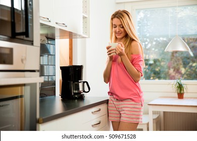 Attractive woman dressed in pyjamas in the kitchen pouring a mug of hot filtered coffee from a glass pot. Having breakfast in the morning - Powered by Shutterstock