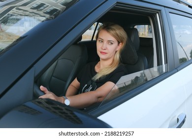 Attractive Woman Driving A Car. A Blonde Woman With Bright Make-up Is Driving A Car. Portrait Of A Serious Woman.