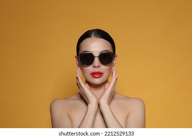 Attractive Woman In Fashionable Sunglasses Touching Face Against Orange Background