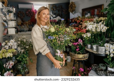 Attractive woman flower shop owner in apron holding bouquet of flowers at florist store - Powered by Shutterstock