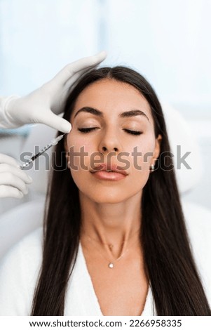 Attractive woman is getting a rejuvenating facial injections at beauty clinic. The expert beautician is filling female wrinkles with botulinum toxin injections or hyaluronic acid fillers.