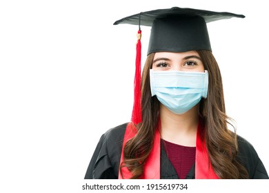 Attractive Woman In Her 20s With A Graduation Cap And A Face Mask Against A White Background. Pretty Female Graduate Attending Her Graduation Ceremony During The Covid Pandemic