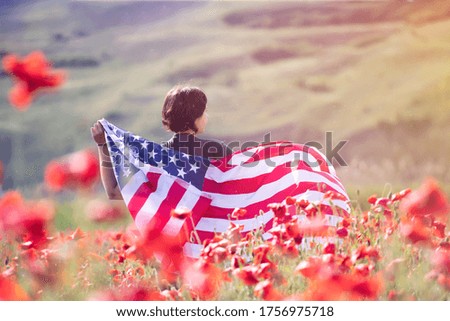 Attractive woman holding Flag of the United States in beautiful summer field on a clear, sunny day. Celebrating Independence Day, National holiday concept.