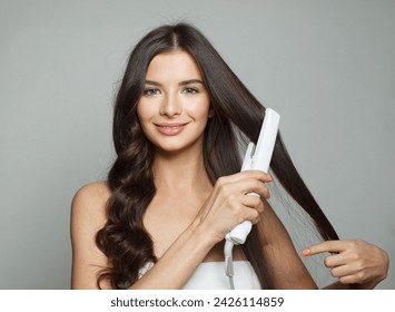 Attractive woman holding hair iron and straightening her healthy long dark hair on white background. Haircare and hair styling concept - Powered by Shutterstock