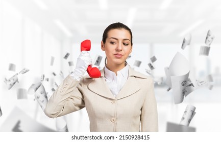 Attractive Woman Holding Vintage Red Phone In Office With Flying Paper Documents. Elegant Operator In White Business Suit Posing With Telephone. Hotline Telemarketing And Business Communication.