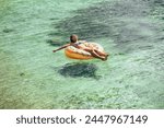 An attractive woman is leisurely floating on an inner tube in the ocean water, relaxed and enjoy on vacation.