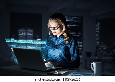 Attractive Woman Looking At Her Laptop Screen Sitting In Night Office. Mixed Media