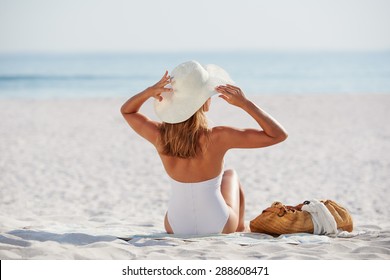 Attractive Woman Looking At View Sitting On Beach Wearing One Piece Bathing Suite