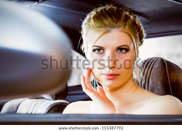 An attractive woman looks at herself in the driving\
mirror  