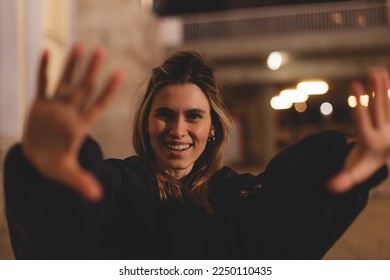 Attractive woman with a lovely smile making a frame gesture with her fingers framing her face. Woman posing on selfie photo looking at camera walking outdoors in urban city at night or evening. - Powered by Shutterstock